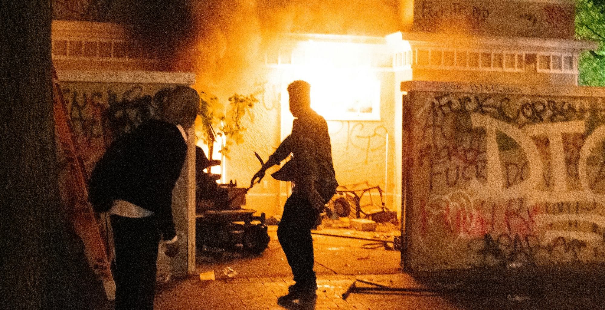 A figure in front of a burning building at night
